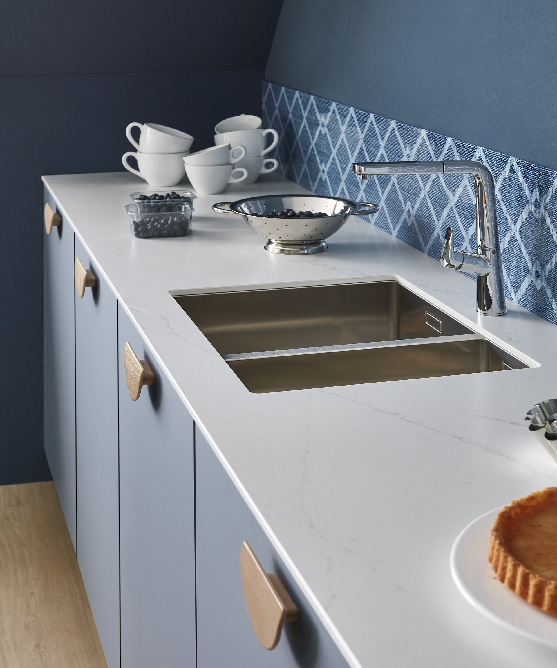Küchenzeile mit Marmor-Arbeitsplatte pastellgraublaue Fronten Holzgriffe blau gemusterter Spritzschutz niedrig